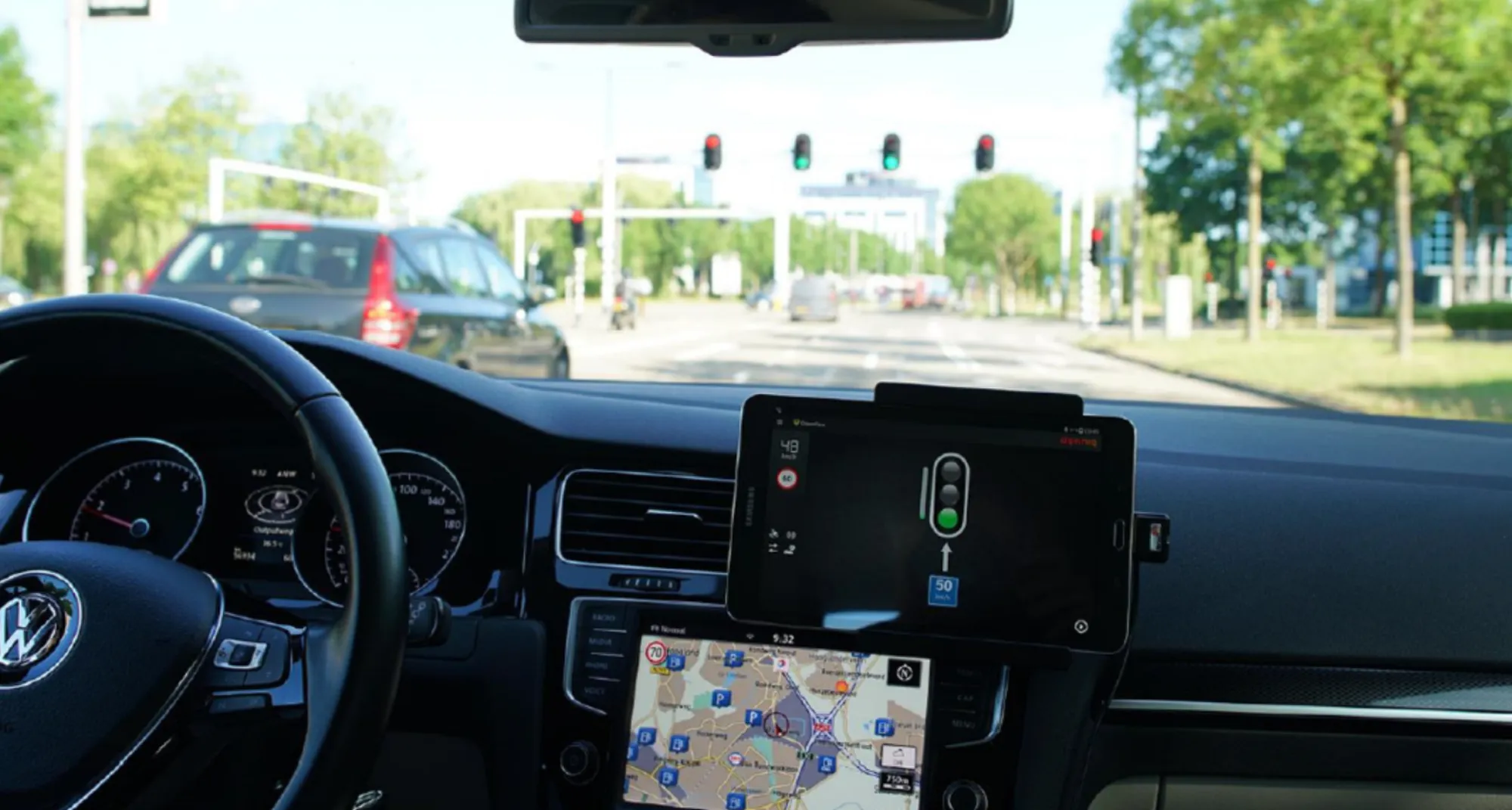 Tablet on a car dashboard with the app showing a green light, with a junction with traffic lights ahead