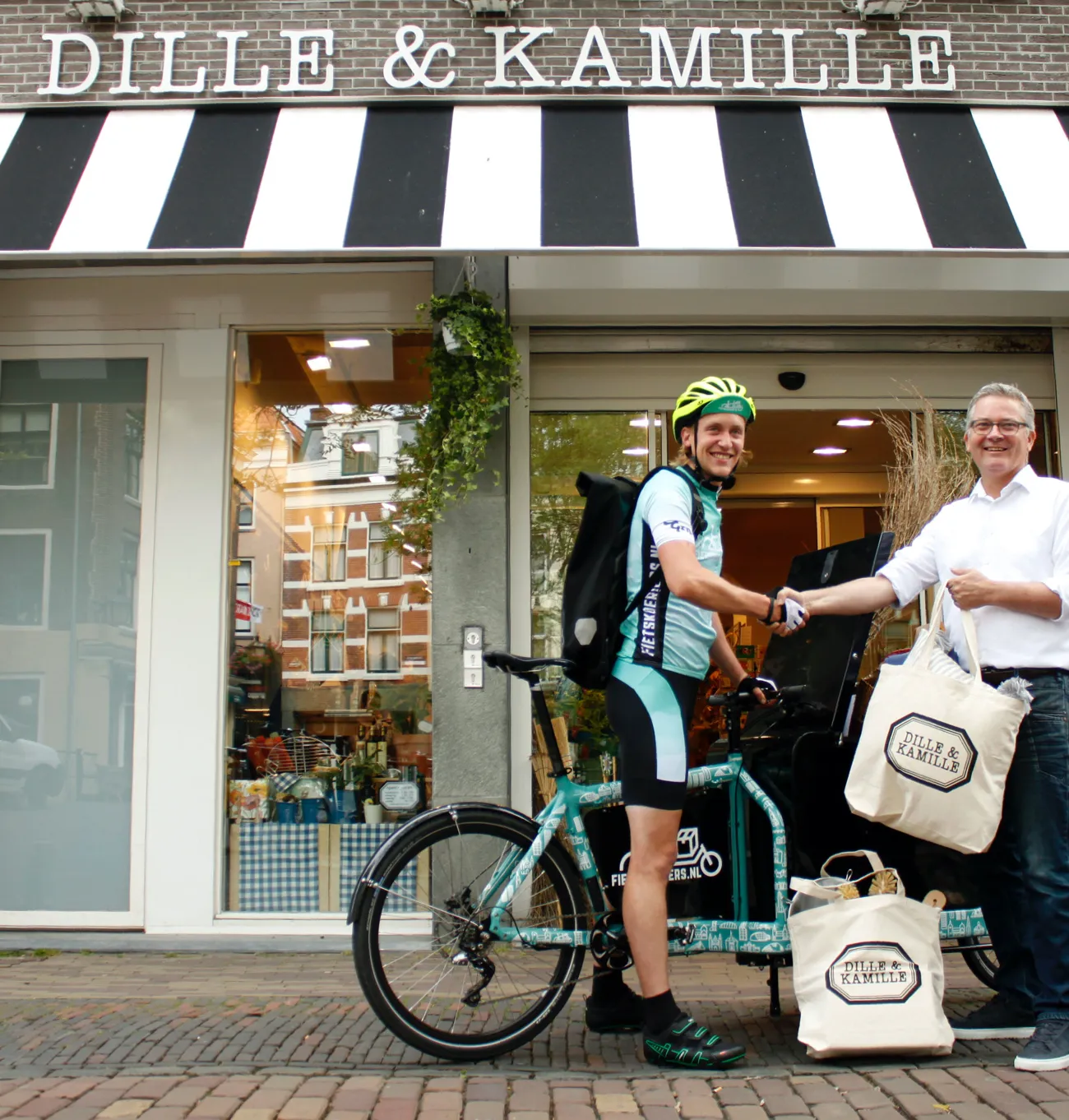 Bike courier with a cargo bike shaking hands with a man holding Dille & Kamille bags in front of a Dille & Kamille shop